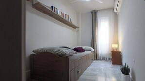A modern bedroom with a wooden bed, a bedside table with a lamp, a small potted plant, and a shelf with books.