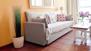 Ein Wohnzimmer mit einer Couch, einem Couchtisch, einer Topfpflanze, einem Spiegel und einem Fenster mit Vorhängen.