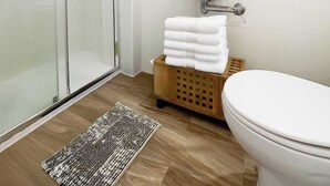 Ein Badezimmer mit Duschabtrennung aus Glas, einem Waschbecken mit Spiegel darüber, einer Toilette und einem kleinen Holzkorb mit Handtüchern.