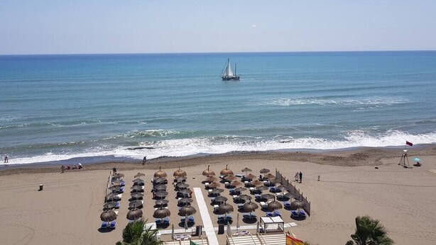 A beach with rows of sun umbrellas and lounge chairs, a sailboat in the distance, and a clear view of the ocean. - Cristamar Center and Beach Penthouse (Estepona)