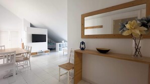 A modern living room with a dining area, a TV mounted on the wall, and a wooden console table with a vase of flowers. - Cristamar Center and Beach Penthouse (Estepona)
