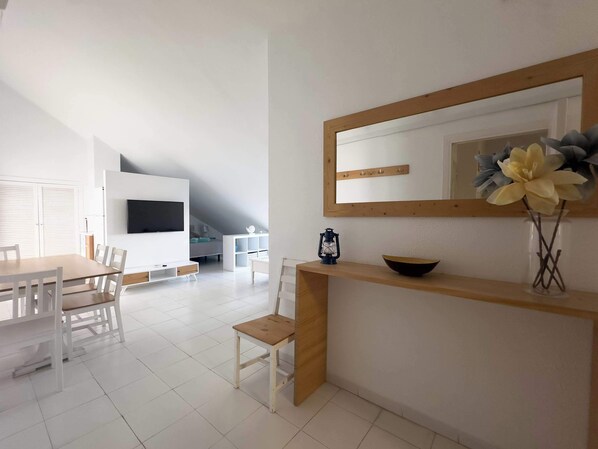 A modern living room with a dining area, a TV mounted on the wall, and a wooden console table with a vase of flowers.
