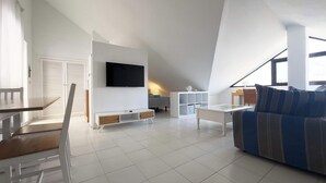 A modern living room with a flat-screen TV, a sofa, a dining table, and a staircase leading to an upper level. - Cristamar Center and Beach Penthouse (Estepona)