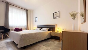 Une chambre d’hôtel avec un lit, des tables de chevet, une chaise, un bureau et un vase avec des fleurs.