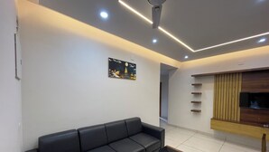 Un salon moderne avec un canapé en cuir noir, une table basse en verre, un éclairage encastré au plafond et un meuble TV en bois.