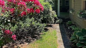 Une maison dotée d’un porche abrité, d’un chemin menant à l’entrée, ainsi que de divers arbustes et plantes.