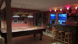 Une table de billard avec des tabourets, un coin bar et des tableaux encadrés aux murs.