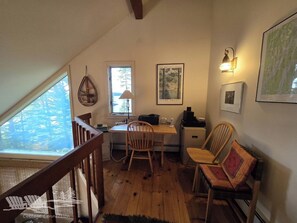 A cozy room with a wooden desk, two chairs, a lamp, and framed pictures on the walls.