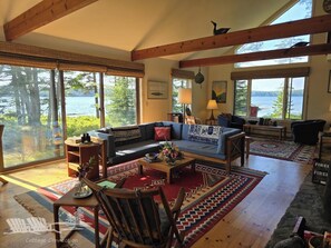 A cozy living room with a large window overlooking a lake, furnished with a sofa, chairs, and a coffee table.