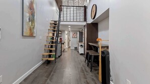 A hallway with a wooden staircase, a black standing fan, and a clock on the wall. - Updated Loft in a Convenient Area! (Wheat Ridge)