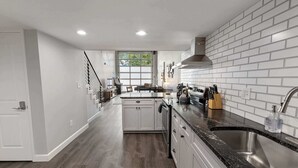 A modern kitchen with white cabinetry, a black granite countertop, and a stainless steel sink. - Industrial-Chic Loft with King Bed Close to Shops! (Wheat Ridge)