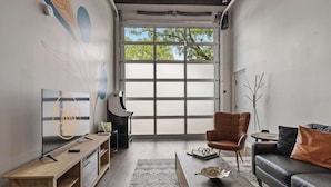 A modern living room with a large window, a sofa, a coffee table, and a TV on a wooden stand. - Industrial-Chic Loft with King Bed Close to Shops! (Wheat Ridge)