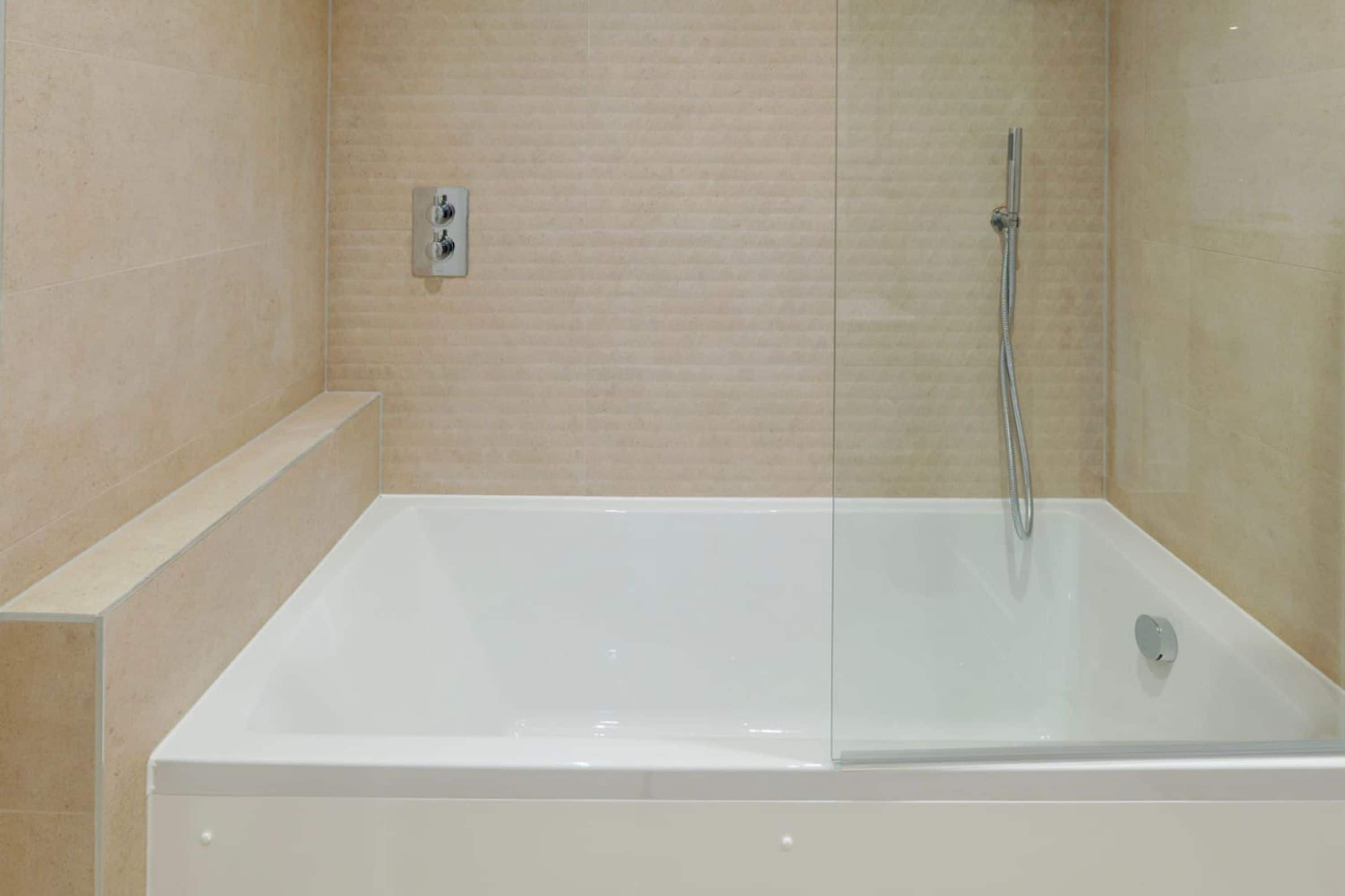 A modern bathroom with a glass-enclosed bathtub, a showerhead, and a control panel on the wall.