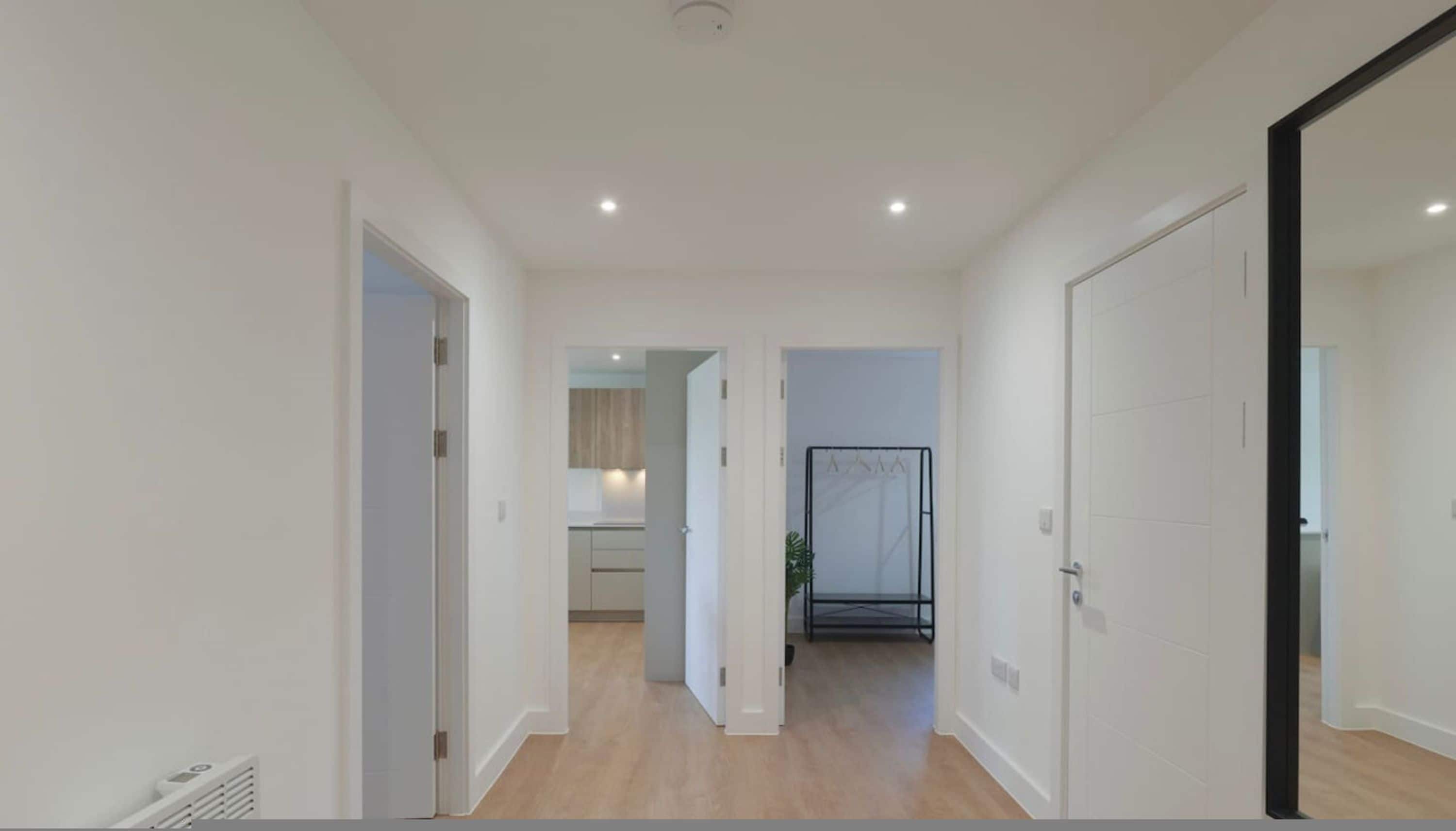 A hallway with white walls and wooden flooring leading to a kitchen area with cabinets and a countertop.