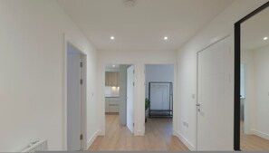 A hallway with white walls and wooden flooring leading to a kitchen area with cabinets and a countertop. - Luxury Manchester Apartment - Blue (Cheadle)