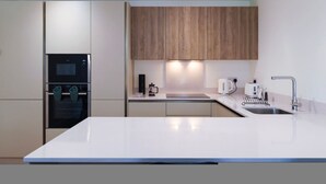 A modern kitchen with white cabinetry, a built-in oven, a coffee maker, and a sink.