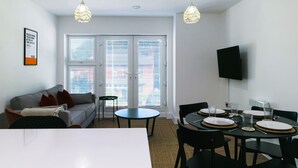 A modern living room with a sofa, a dining table set for four, and a television mounted on the wall.