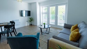 Un soggiorno moderno con un divano grigio, una poltrona blu, un tavolino rotondo e una TV a schermo piatto fissata al muro.