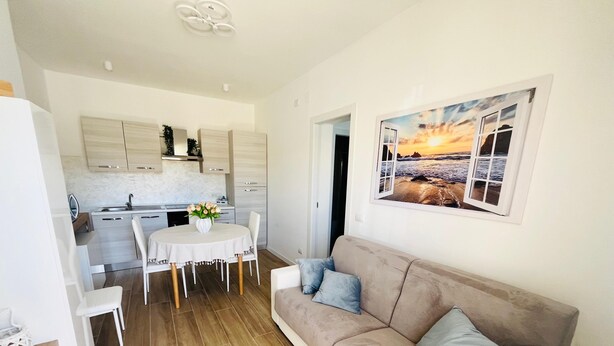 A compact living space with a dining area, kitchenette, and a sofa with cushions. - Apartment in beachfront residence (Alghero)