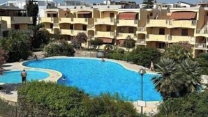 A hotel with multiple balconies, a swimming pool, and surrounding greenery. - Apartment in beachfront residence (Alghero)