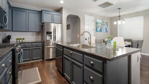 Une cuisine moderne avec des meubles de couleur sombre, des appareils en acier inoxydable et un grand îlot central doté d’un évier.