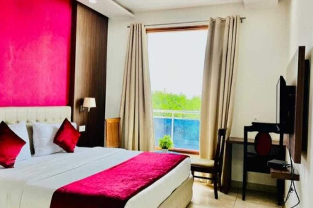 Une chambre d’hôtel avec un lit, un bureau, une chaise, une télévision et une fenêtre avec des rideaux.