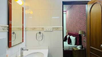 A bathroom with a sink, mirror, and towel rack. The room has a brick wall and a wooden door.