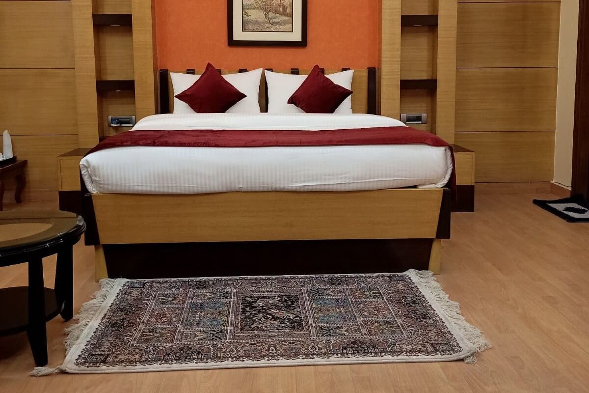 Un lit bien fait, recouvert d’une couvre-lit rouge et blanche, un tapis à motifs et un tableau encadré accroché au mur.