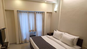 Habitació d'hotel amb un llit, cortines, una taula de nit amb una làmpada i una televisió sobre un suport.