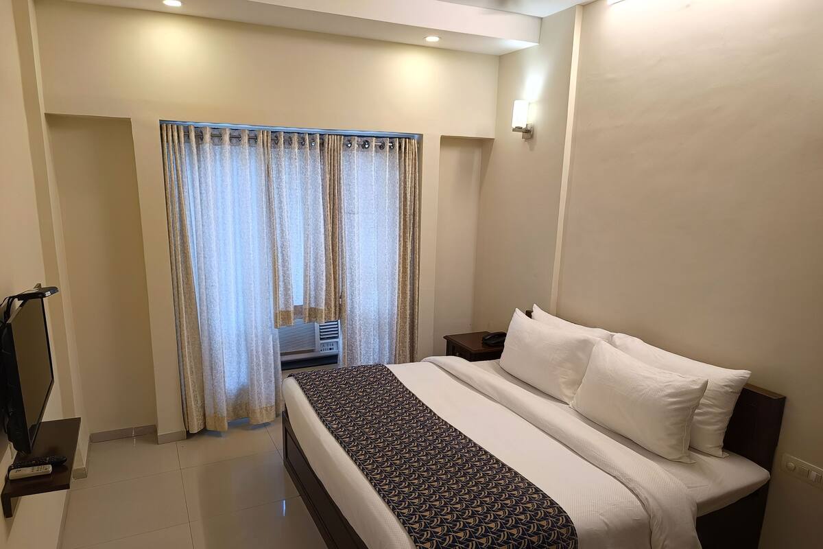 A hotel room with a bed, curtains, a bedside table with a lamp, and a television on a stand.