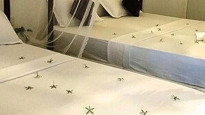 A bed with a mosquito net, white bedding with star patterns, and a bedside table with a book.