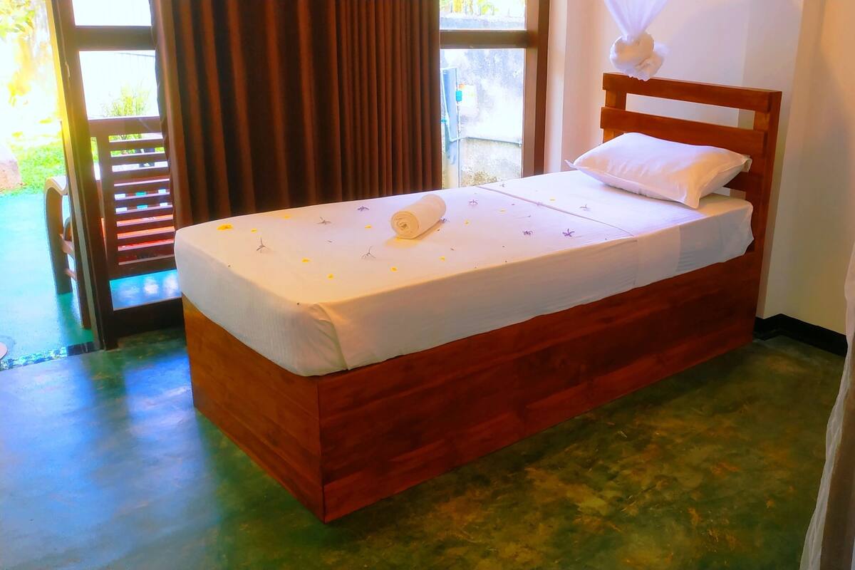 Una cama individual con estructura de madera, ropa de cama blanca y una toalla enrollada sobre la cama.
