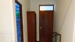 A narrow hallway with a wooden door at the end, a small wooden stool, and a white door on the left.