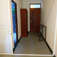 Un pasillo estrecho con una puerta de madera al final, un taburete pequeño de madera y una puerta blanca a la izquierda.