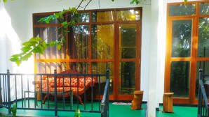 A covered outdoor seating area with a bench and a table, surrounded by a green railing and steps leading up to a door.