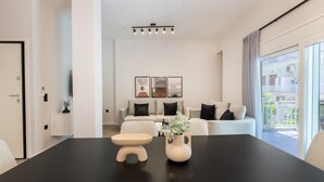 A modern living room with a black dining table, a beige sofa set, and a large window with a view of the outside. - Lovely 3BR Apartment in Pangrati (Kesariani)