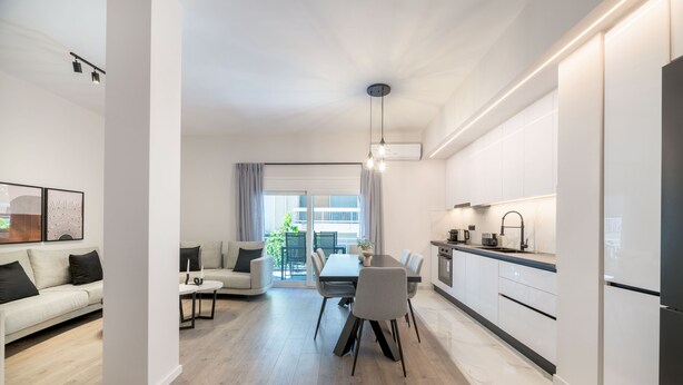 A modern kitchen with white cabinets, a dining area with a table and chairs, and a living room with a sofa and a coffee table. - Lovely 3BR Apartment in Pangrati (Kesariani)