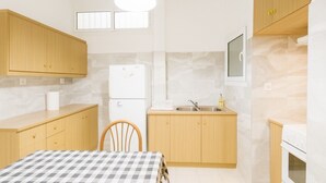 A compact kitchen with wooden cabinets, a refrigerator, a sink, and a dining table with a checkered tablecloth. - Sunny Dream House (Agios Ioannis Rentis)