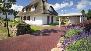 A house with a thatched roof, a stone wall, and a garden with lavender. - Ferienhaus, Fuhlendorf (Fuhlendorf)