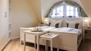 A bedroom with a bed, bedside tables, a window with curtains, and a small table with a teapot and cups. - Ferienhaus, Fuhlendorf (Fuhlendorf)