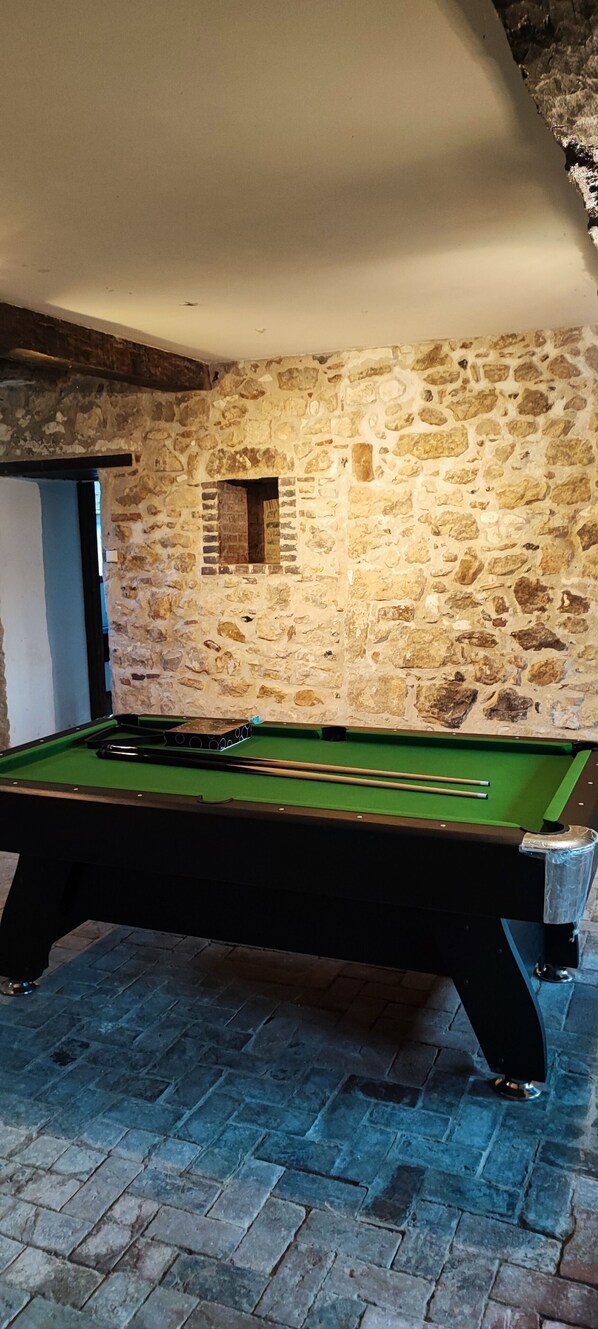 A pool table with a stone wall backdrop, a door to the left, and a tiled floor. - 12th-century Manoir des Templiers, with a heated pool, hot tub, and mini-golf course (Trancault)