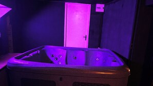 A hot tub in a room with wooden flooring and a door in the background. - 12th century Manoir des Templiers, with heated swimming pool, jacuzzi, mini golf course  (Trancault)
