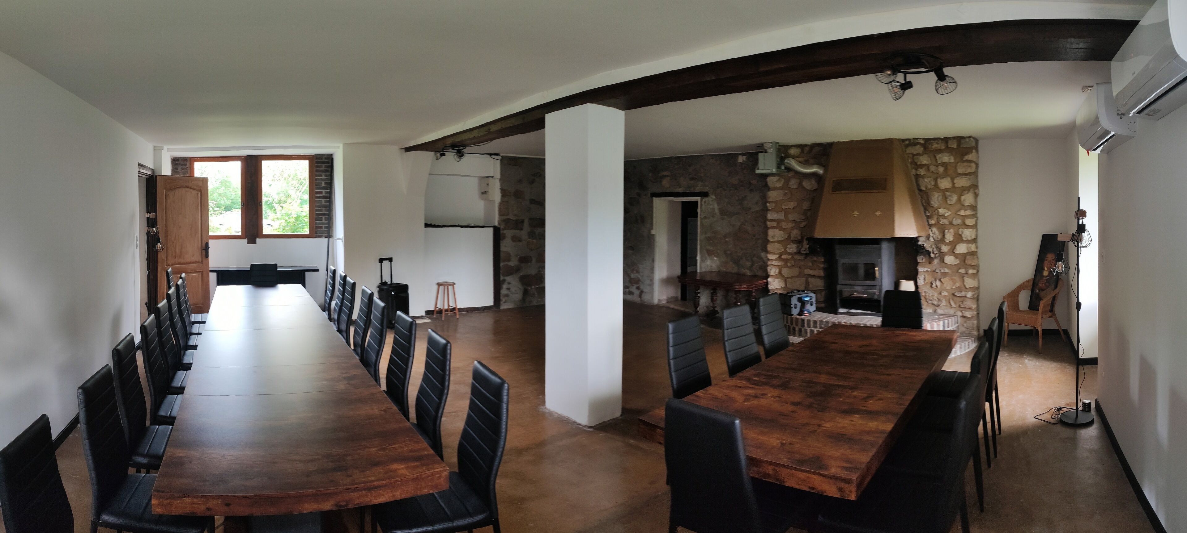 Un vaste espace dédié à la salle à manger, avec une longue table en bois et des chaises noires, un mur en pierre et une cheminée.