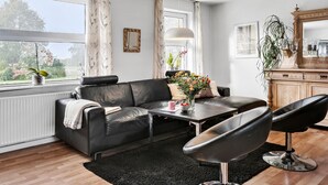 Un salon moderne avec un canapé en cuir, une table à manger et une chaise noire. On y trouve une fenêtre avec des rideaux, un miroir et une plante posée sur le rebord de la fenêtre.