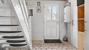 Un couloir étroit avec une porte blanche, un escalier et un petit tapis.