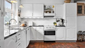 Une cuisine avec des meubles blancs, une cuisinière, un évier et une fenêtre.