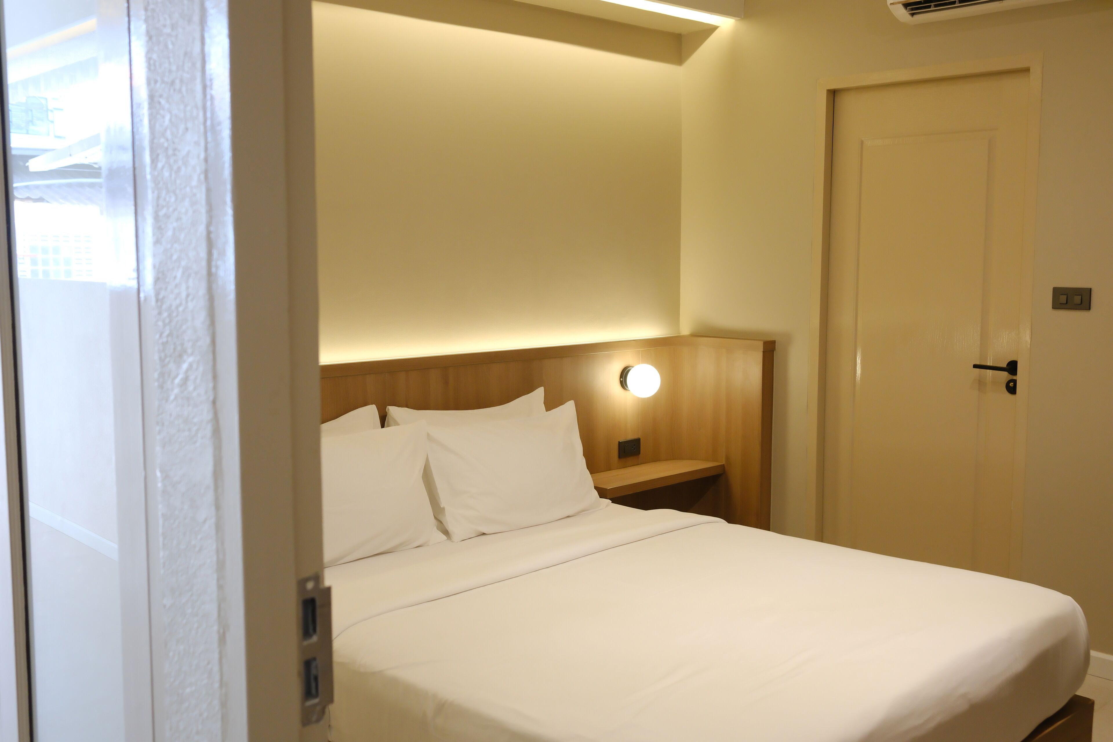 Ett hotellrum med en säng, ett sängbord, ett litet bord och en väggmonterad lampa.