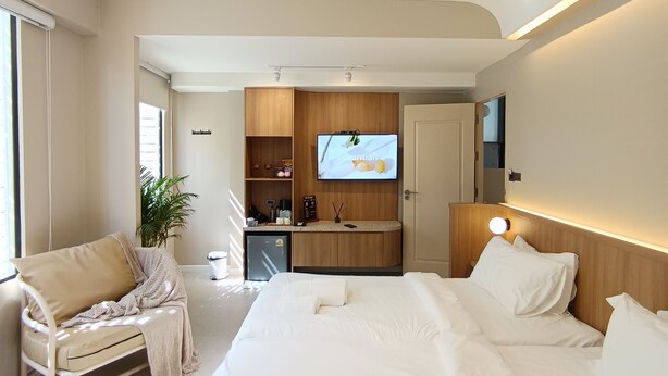 A modern hotel room with a large bed, a seating area with a sofa and armchair, a small kitchenette, and a television. - Urban Room Samed (Rayong)