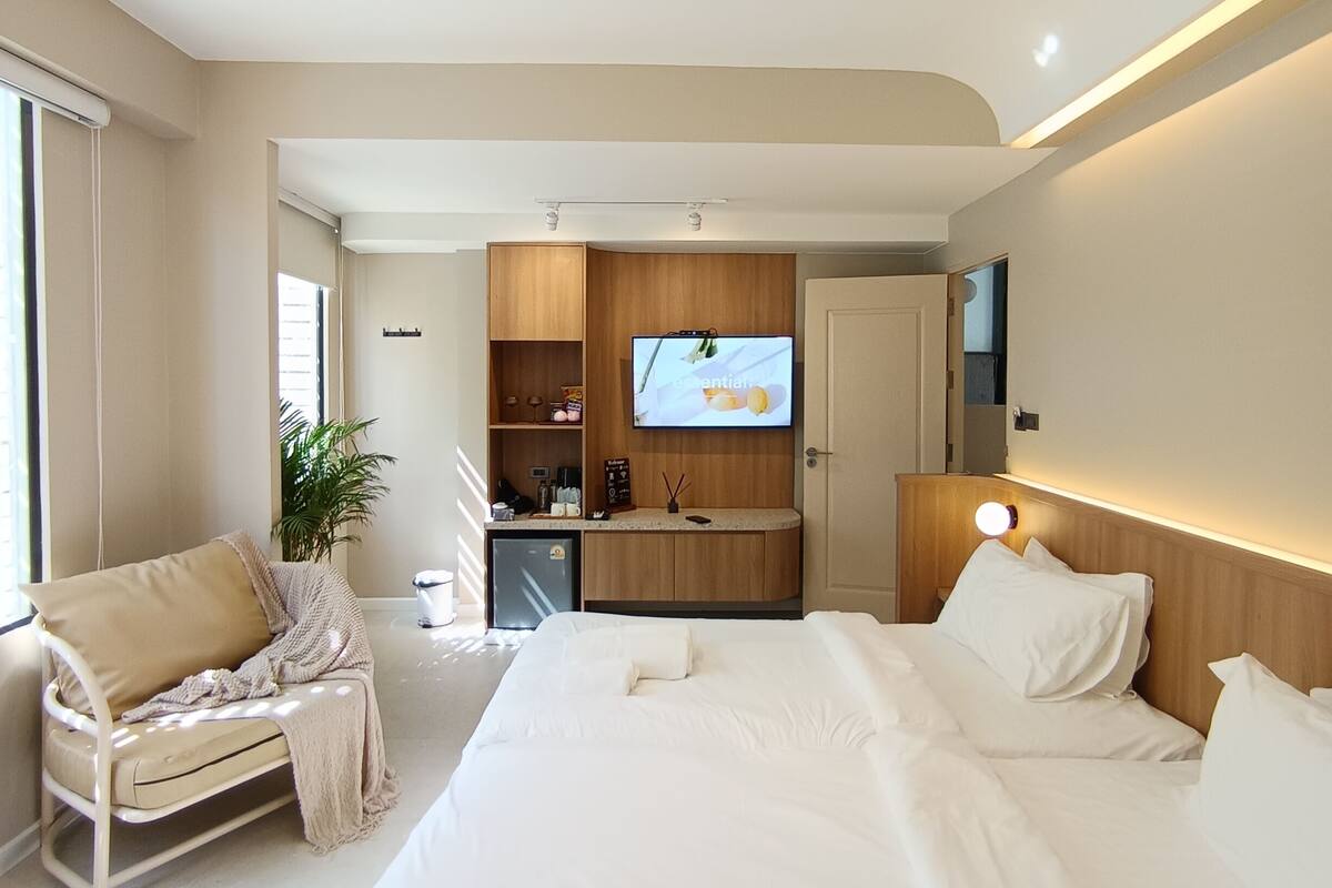 Una habitación de hotel moderna con una cama grande, una zona de estar con sofá y sillón, una kitchenette pequeña y un televisor.