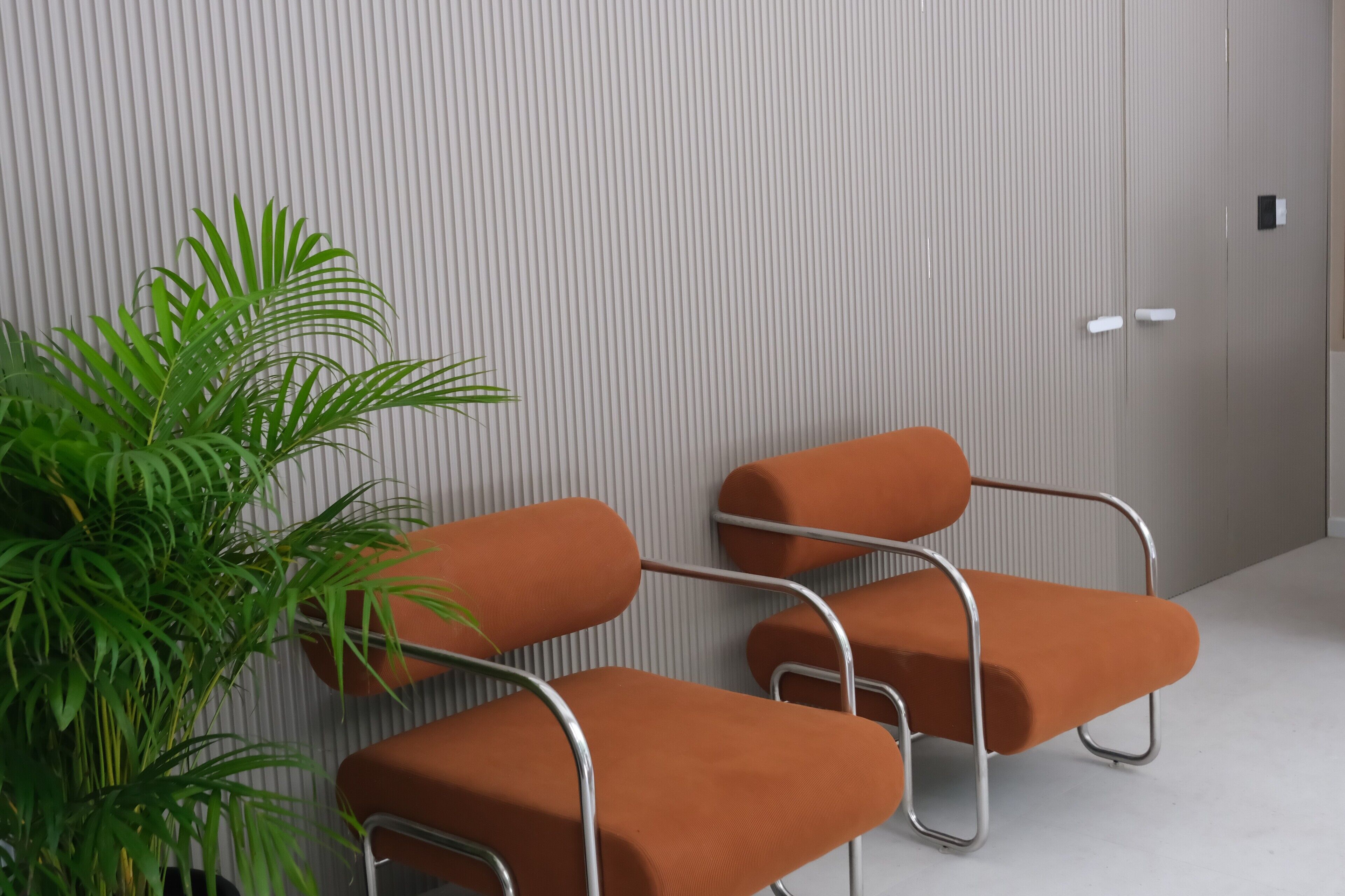 A waiting area with two orange chairs and a potted plant.
